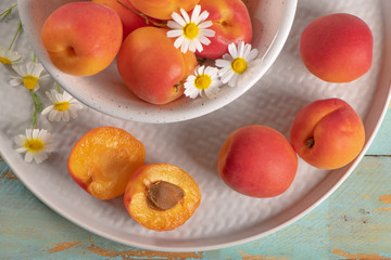 Delicious ripe apricots in a bowl on the wooden table. Close-up with apricots and daisy flowers