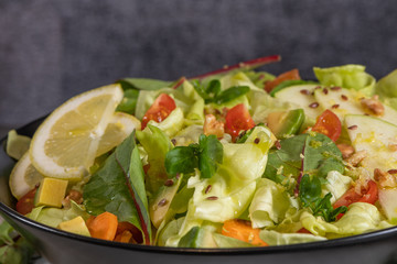 Salad. Spring vegetable salad. Fresh vegetable salad with tomatoes, apple, nuts, seeds and lemon. Olive oil pouring into bowl of salad