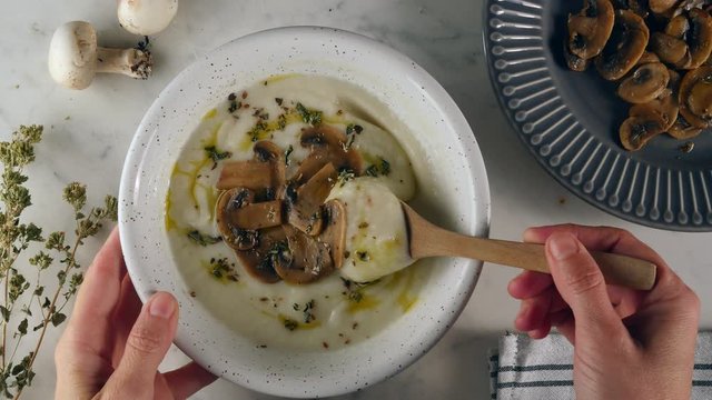 Healthy eating, stirring mushroom soup in a bowl. Eating creamy and rustic white soup with mushroom. Eating healthy vegetarian dinner. Cozy and warm food. Autumn warm puree.