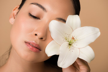 beautiful asian girl holding white lily near face isolated on beige