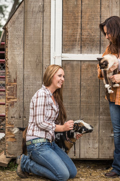 Young western girl on a ranch petting a goat standing next to mother. Bridger, Montana, USA