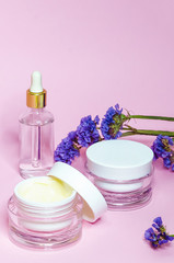 Obraz na płótnie Canvas beauty concept. vertically. jars, bottles with natural cosmetics, cream, serum on a pink background with purple flowers, copy space, soft focus