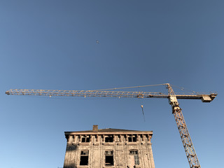 Yellow construction crane and reconstruction of old buildings, blue sky background