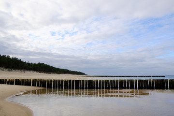 Breakwaters on the beach and beautiful blue sky with clouds in Dziwnowek / Poland on the Baltic Sea.