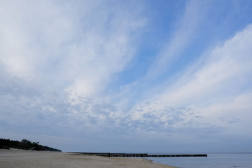 Breakwaters on the beach and beautiful blue sky with clouds in Dziwnowek / Poland on the Baltic Sea.