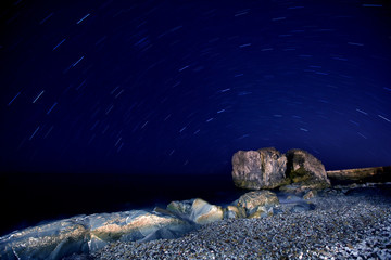 Beach with boulders and seaweed and break on them at night in moon light