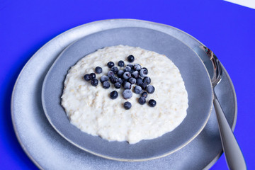 Oat meal with blackberry in gray plate with spoon on blue background