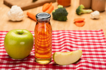 Selective focus of bottle of apple juice and baby food in jars with ingredients on tablecloth on wooden background