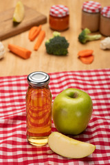 Selective focus of bottle with apple juice and jars of baby food with ingredients on tablecloth on wooden surface