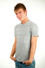 Obraz premium Portrait of a Caucasian young positive guy in a gray shirt and jeans posing on a gray background. Concept of a successful young student or novice employee. Advertising space