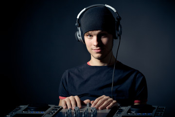 Close-up portrait of a young stylish DJ guy with headphones and musical equipment against a dark background. Concept of professional DJing and music lovers