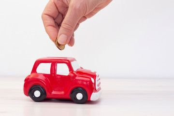 hand puts a coin into a piggy bank in the form of a car. copyspace. The accumulation of money to buy a car. Saving money for a dream. Buying a car.