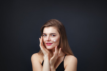 Lovely woman with smooth healthy skin applying cream on her face