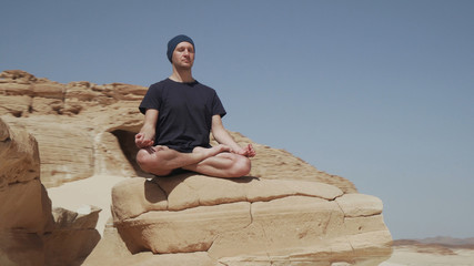 Handsome male sitting in lotus pose on a rock in desert