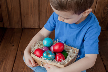 Fototapeta premium Happy baby boy with a basket of easter eggs on wooden background