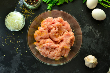 Cooking process. Meat, eggs, spices, parsley,  onions in a glass bowl. Ingredients for Meatballs. Top view. Food and ingredients on a dark table background. Minced chicken.