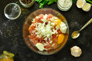 Cooking process. Meat, eggs, spices, parsley,  onions in a glass bowl. Ingredients for Meatballs. Top view. Food and ingredients on a dark table background. Minced chicken.