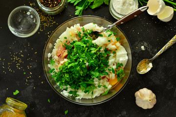 Cooking process. Meat, eggs, spices, parsley,  onions in a glass bowl. Ingredients for Meatballs. Top view. Food and ingredients on a dark table background. Minced chicken.