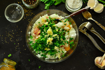 Cooking process. Meat, eggs, spices, parsley,  onions in a glass bowl. Ingredients for Meatballs. Top view. Food and ingredients on a dark table background. Minced chicken.