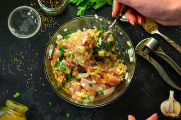 Cooking process. Minced meat and ingredients, salt, pepper, spices, onions, eggs, parsley, mix the ingredients with a spoon. A woman is preparing minced chicken for meatballs. Top view.