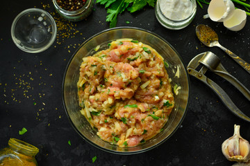 Cooking process. Meat, eggs, spices, parsley,  onions in a glass bowl. Ingredients for Meatballs. Top view. Food and ingredients on a dark table background. Minced chicken.