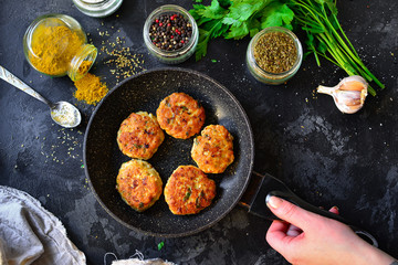 Fried meatballs in a pan. Chicken cutlets in a pan on a dark concrete table background. Top view. Ingredients and cooked meatballs. Spices, parsley, meat dish. A woman holds a pan with food.