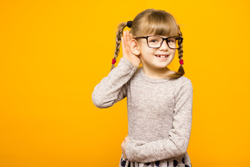 A young child girl journalist in glasses with funny pigtails listening to something holding his...