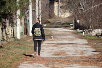 Girl with a backpack is walking along a rural street. Sunny spring weather in a village