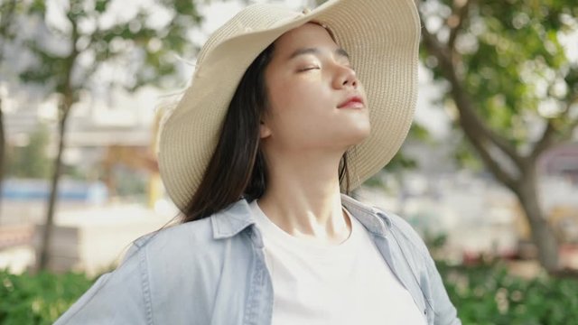 Beautiful asian woman wears a vintage hat relaxed enjoying peaceful sunset and looking up exhaling fresh air relaxing at a public park on the beautiful sunset.