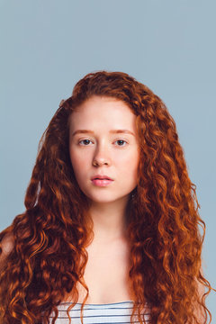 pretty teenage girl with luxurious long curly red hair on a blue background in the studio. Copy space for text
