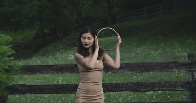 Psychedelic picture. Beautiful Asian girl holds a mirror in her face. In the background is an alpine meadow. The concept of freedom, unity, reflection, existence. Filmed in Raw. 12 bit colors.