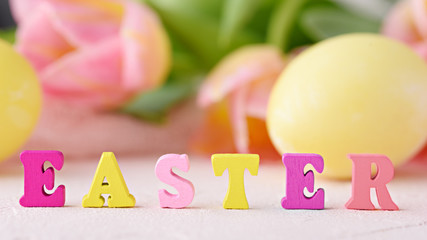 word Easter is made up of multicolored letters on background of flowers and Easter eggs