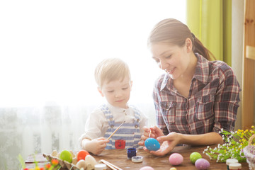 Happy time while painting easter eggs. Easter concept. Happy mother and her cute child getting ready for Easter by painting the eggs