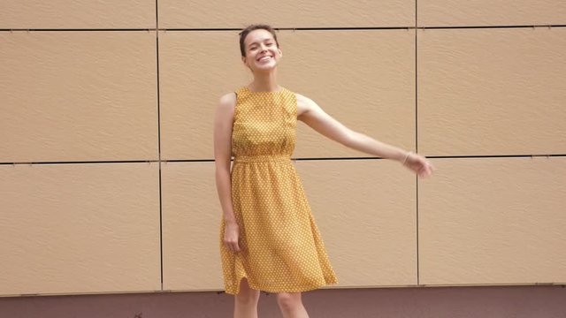 Beautiful smiling brunette model posing near yellow wall in hipster dress. Trendy girl having fun in the street. Funny woman shows positive emotions