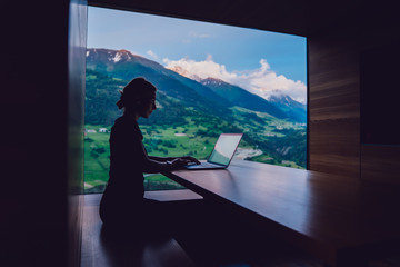 Skilled female digital nomad working remotely creating trip guide to high mountains for share to...