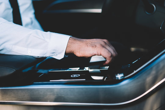Cropped image of male driver shifting power on automotive gear stick choosing speed on transmission of contemporary rent car, selective focus on man steering automobile transport during getaway travel
