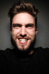 young handsome male with beard, mustache and trendy hairdo, wears casual grey sweater, has serious expression, poses in studio against gray background