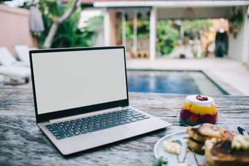 Open laptop and jelly near plate with sandwich on table in yard