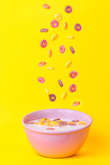 Colored cereals falling in a pink bowl with milk.