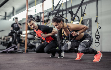 Fototapeta na wymiar Sport. Man and Women training with fitness straps in the gym. Beautiful lady exercising her muscles sling or suspension straps. 