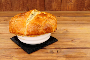 Individual steak and ale pie in a ceramic dish with puff pastry topping on a wooden background