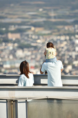 夫婦と子供の3人家族が展望台から風景を見ている。