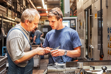 Skilled workers standing in a production hall for electric motors in front of a machine tool,...