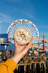 Female hand holding a donut on a background of a ferris wheel on Santa Monica beach