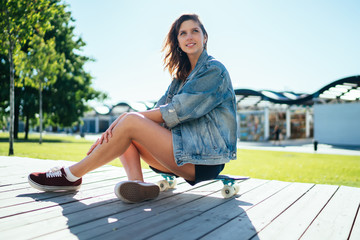 Fototapeta na wymiar Smiling young female sitting on skateboard in city park