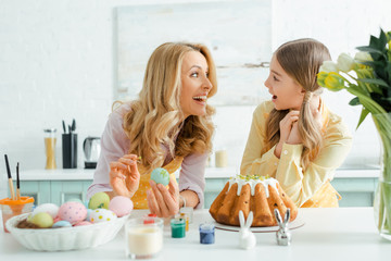 happy money and daughter looking at each other near easter cake, chicken eggs, decorative rabbits...