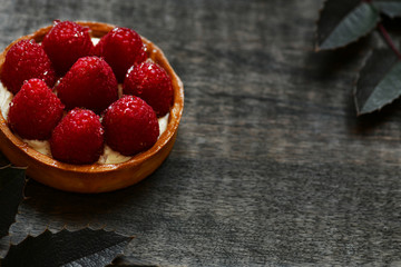 Tartlet with raspberries. Dessert on the dark board. Decoration of dessert with leaflets.