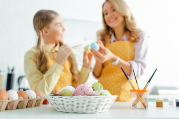 selective focus of basket with painted easter eggs near happy mother and daughter