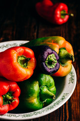 Multicolored fresh bell peppers in bowl over wooden background