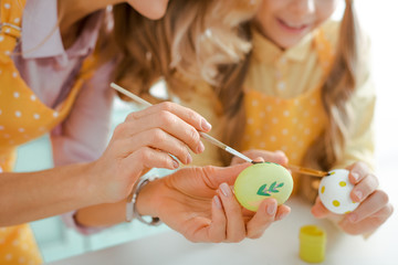 cropped view of mother and daughter painting chicken eggs on easter